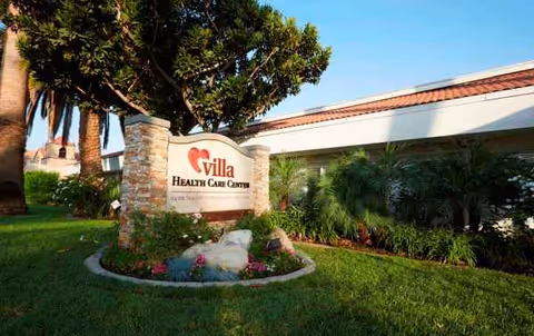 Exterior view of Villa Health Care Center with a landscaped sign and palm trees.