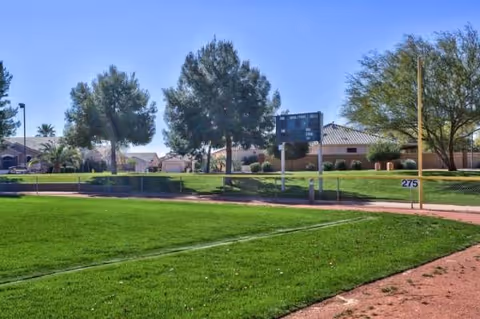 Outdoor view of Arizona Traditions' grassy area with trees and a distant building.