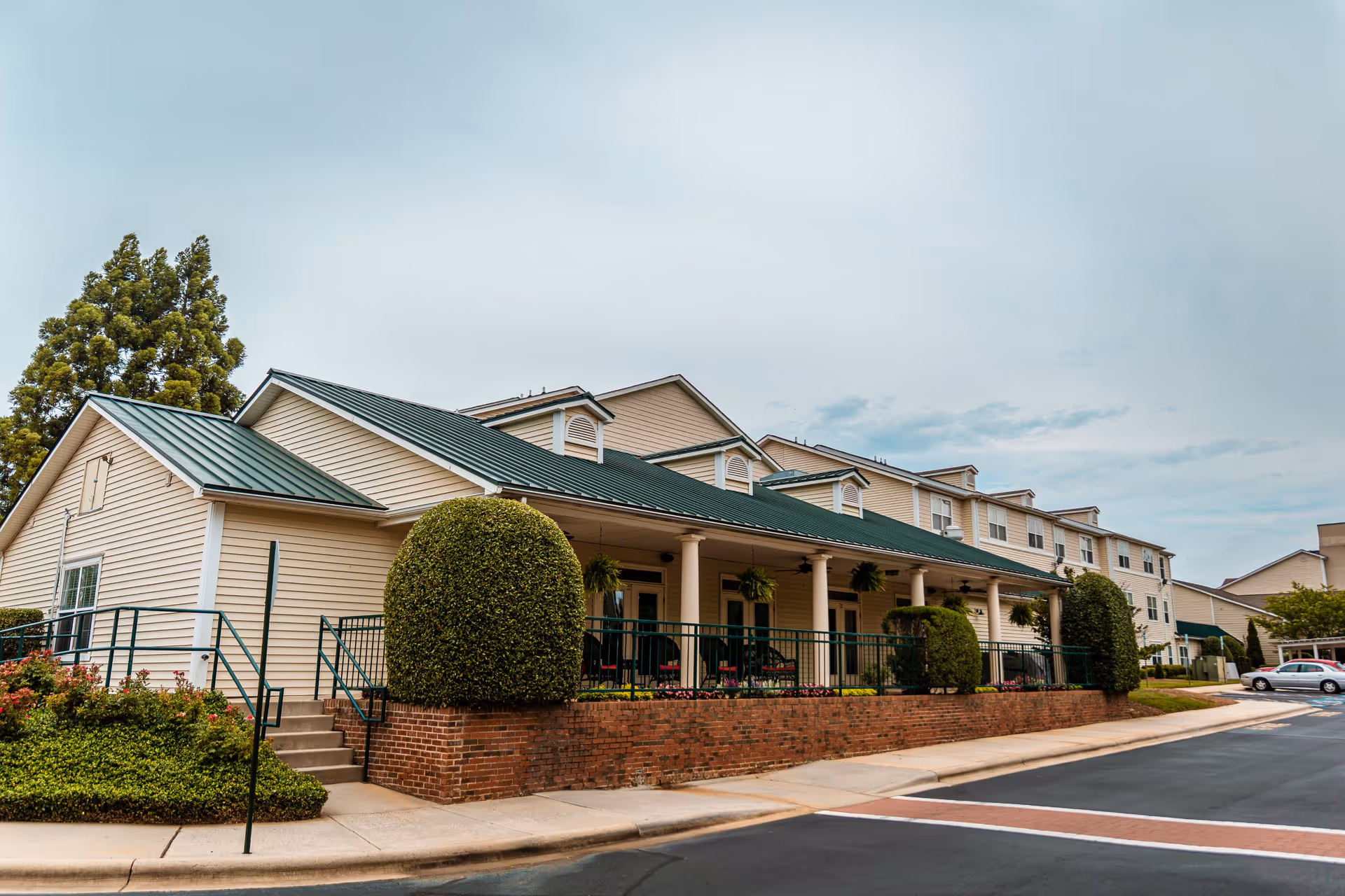 Front exterior of The Dorchester building showing a covered porch with columns, a green metal roof, and manicured landscaping.