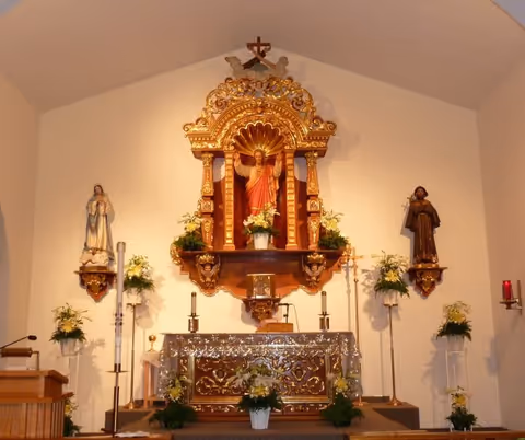 Ornate chapel altar with a central statue of Jesus in a gilded niche flanked by statues, candles, and floral arrangements.