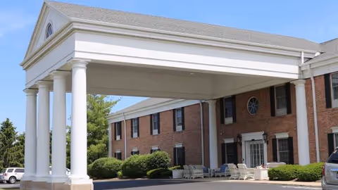 Brick senior living facility with a covered entrance supported by white columns.