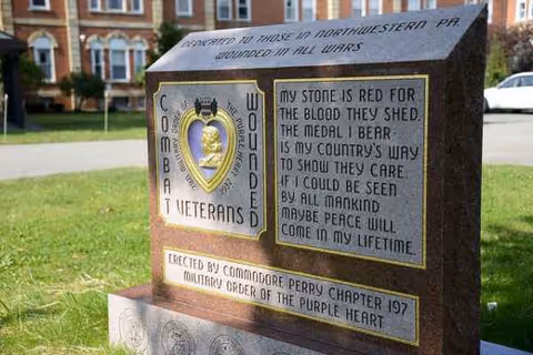 Stone memorial marker on a grassy lawn with a brick building behind.