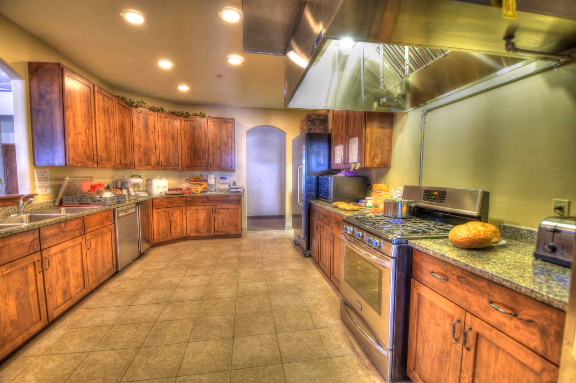 Spacious communal kitchen with wooden cabinets, stainless steel appliances, granite countertops and a tiled floor.