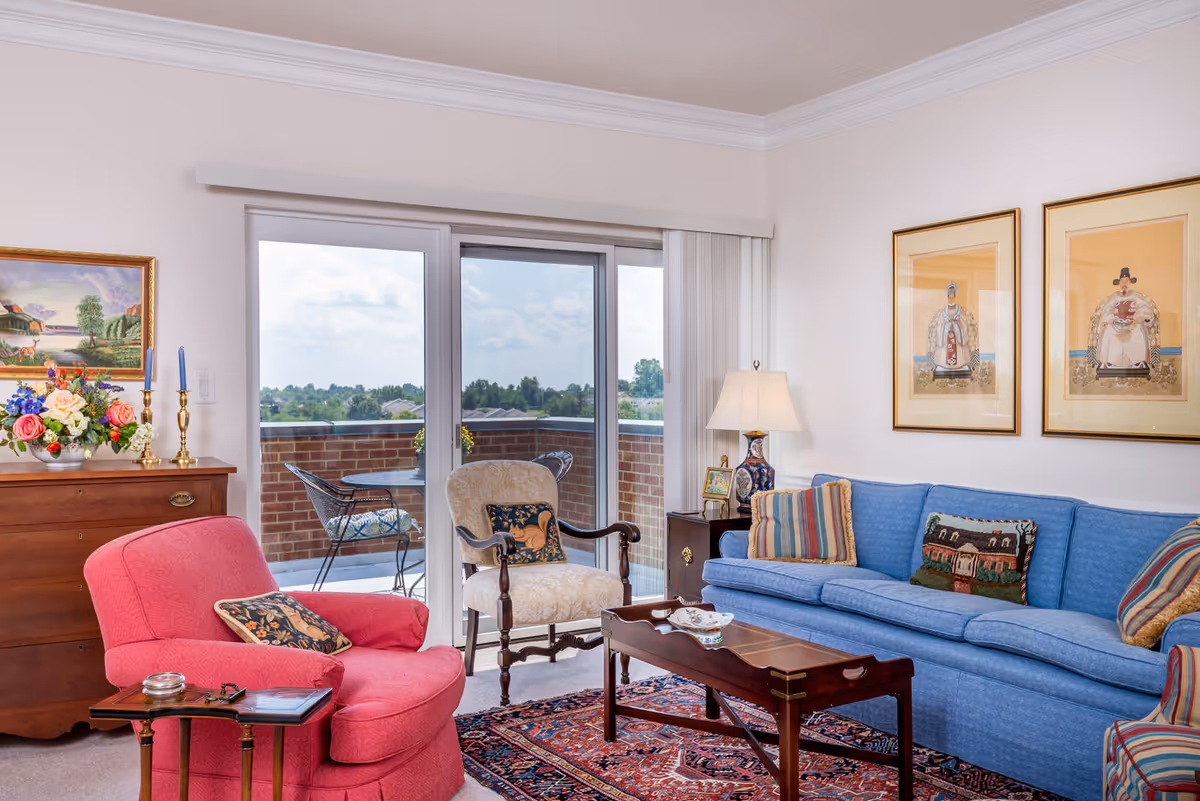 Bright living room with a blue sofa, pink armchair, wooden coffee table, and sliding glass doors opening onto a balcony.