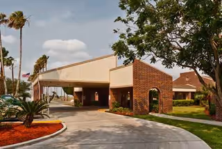 Exterior of Palma Real senior living facility showing brick entrance and palm trees.