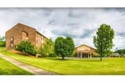 Brick retirement community buildings with a manicured lawn, trees, and a cloudy sky.