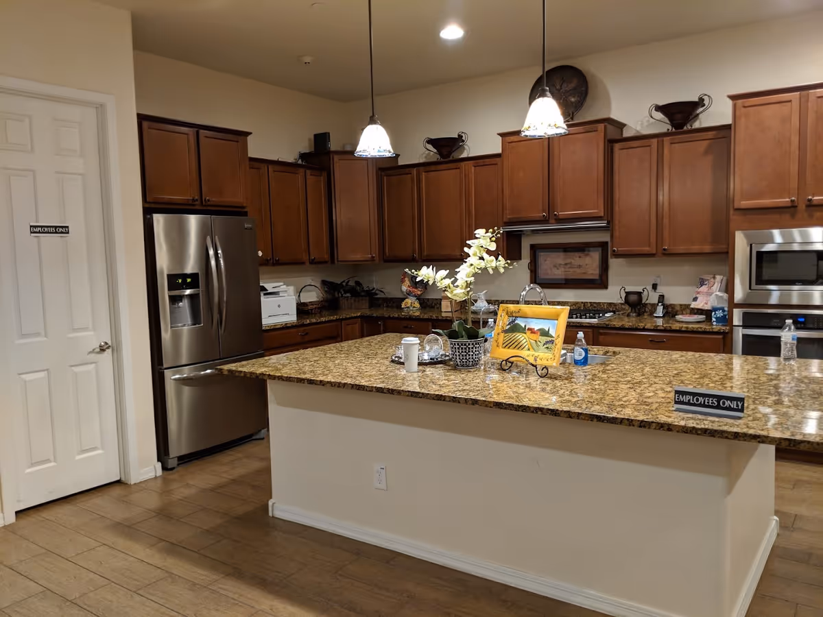 Spacious kitchen with a large granite island, wooden cabinets, stainless steel refrigerator and oven, and pendant lights.