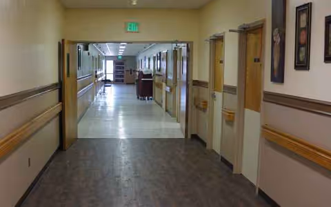 Long hallway inside a senior living facility with doors, handrails, and muted decor.
