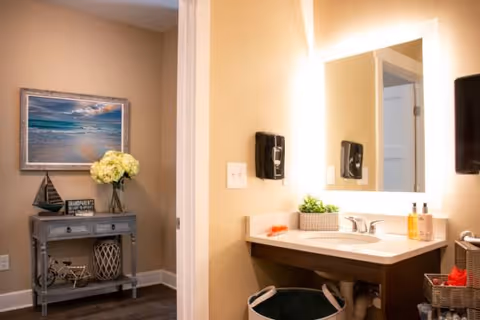 Bright senior living bathroom vanity with mirror and sink; decorative console and wall art nearby.