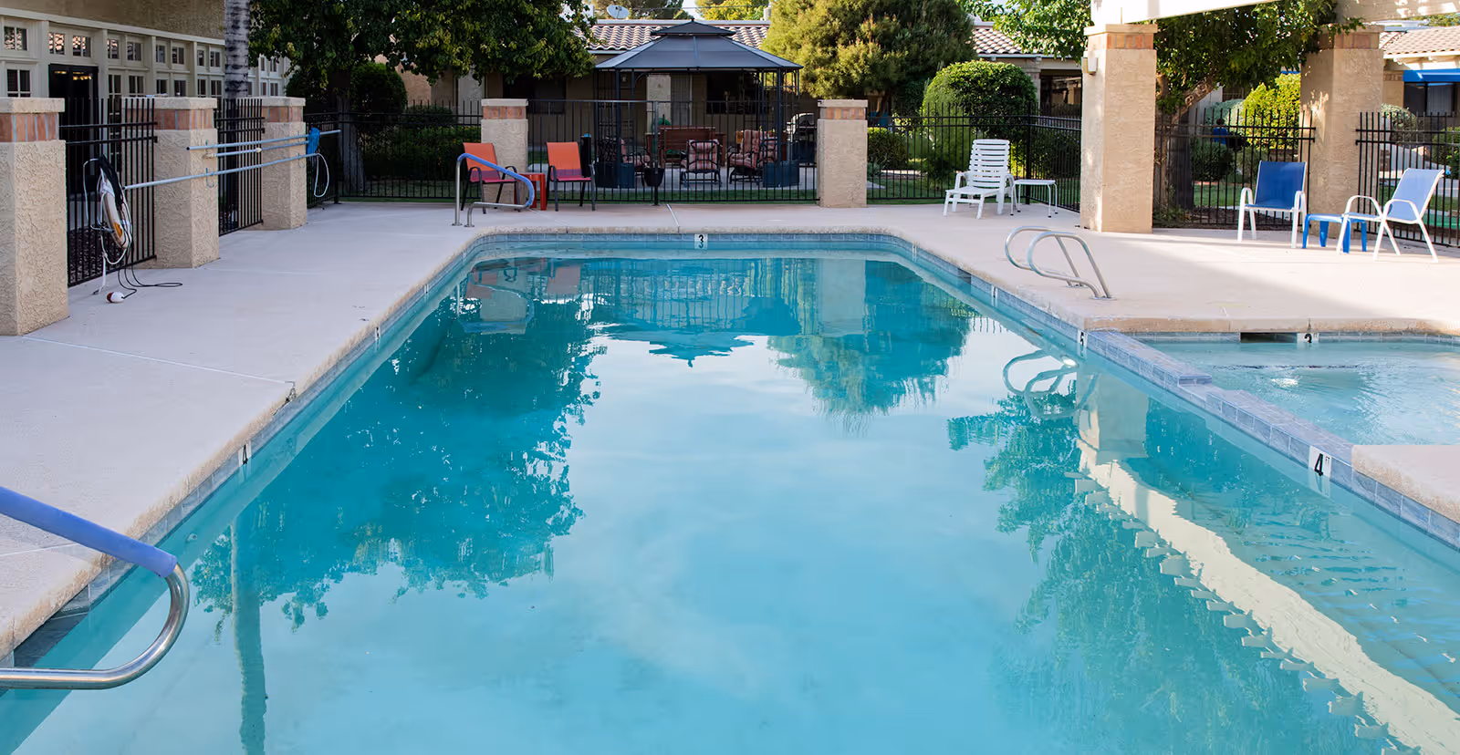 Outdoor swimming pool at a retirement community with lounge chairs, a fenced deck, and surrounding landscaping.