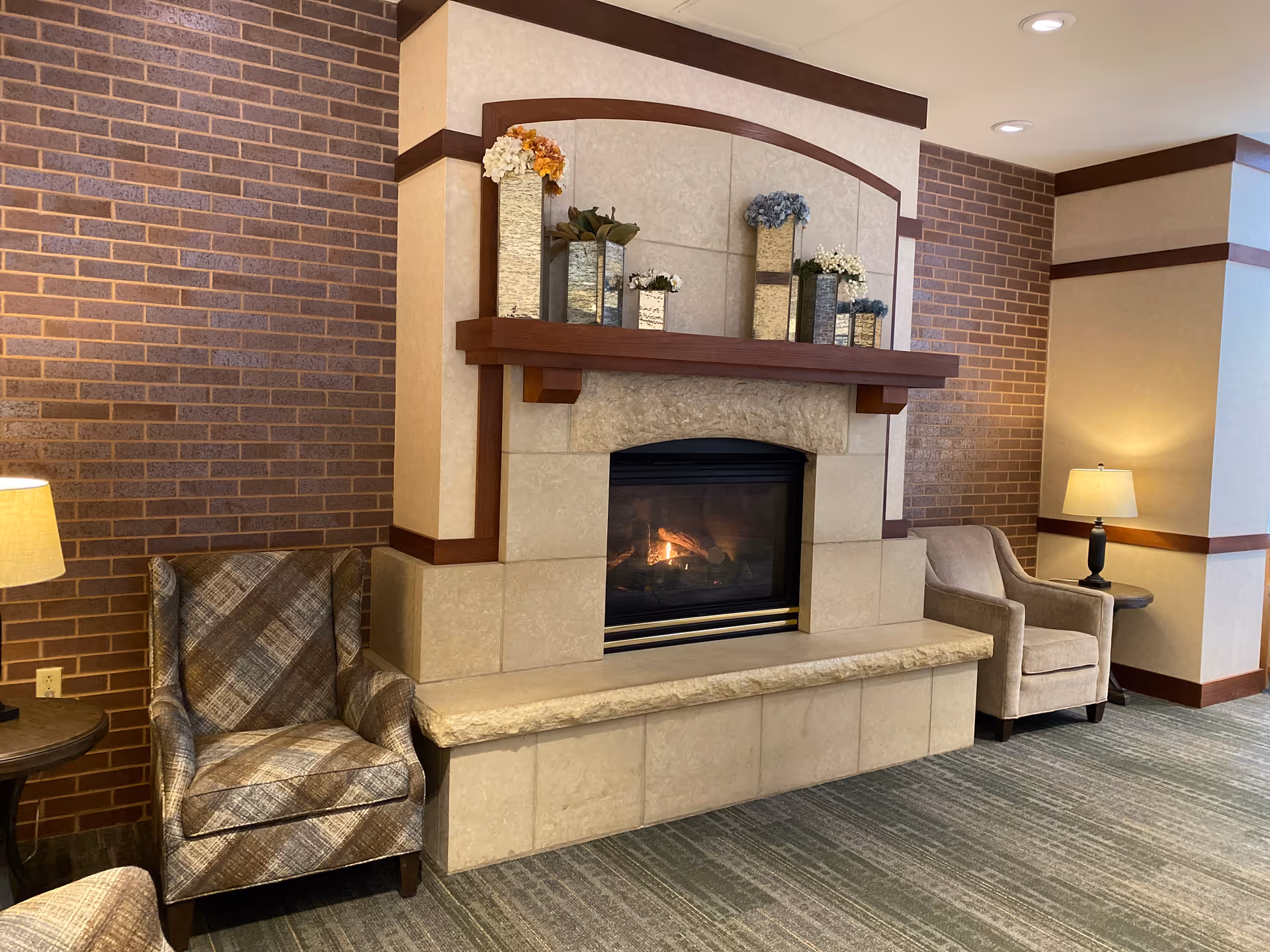 Cozy lounge area with a stone fireplace, decorative mantel, and upholstered armchairs on either side.