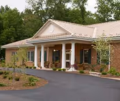 Brick senior living facility exterior with columns, entryway, and surrounding trees.