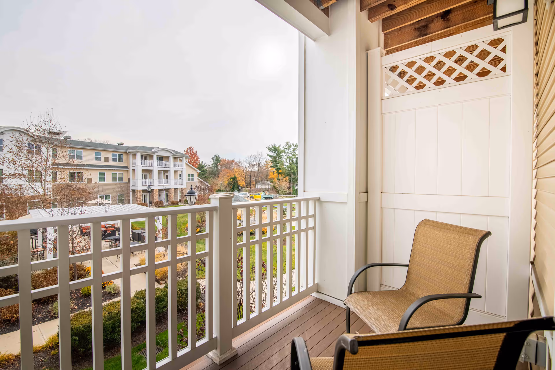 A small balcony with two chairs overlooking a landscaped courtyard and a multi-story senior living building.
