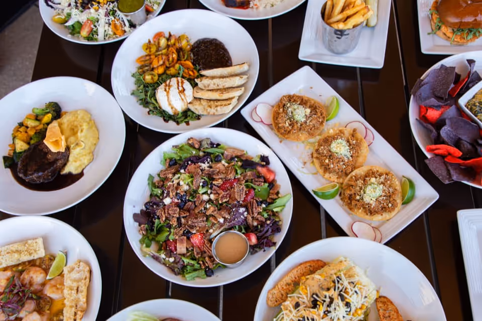 Overhead view of a table filled with assorted plated dishes including salad, tacos, fries, and chips.