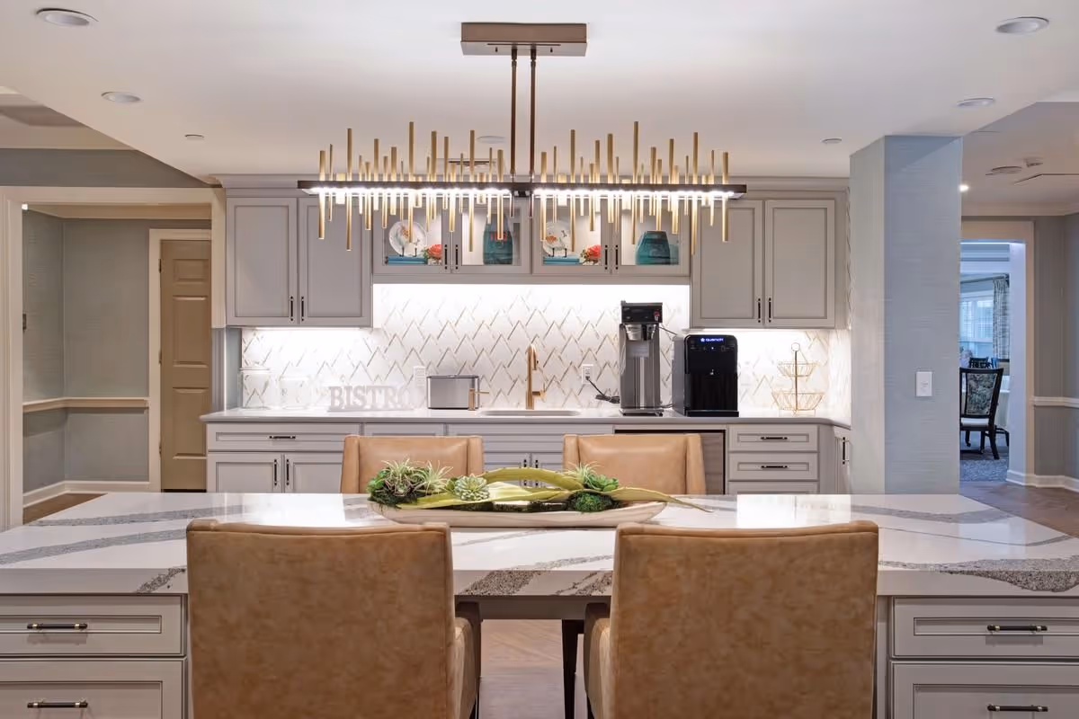 Contemporary kitchen with a large marble island, four leather chairs, a modern chandelier, and a countertop coffee station.