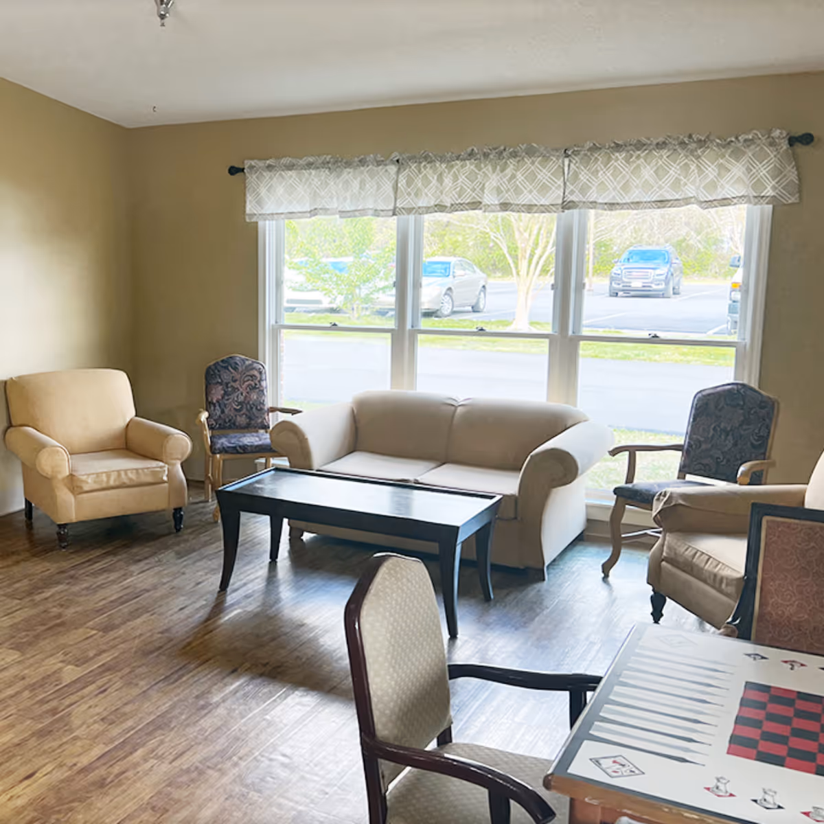Cozy living room in a senior facility with sofa, chairs, and a large window.
