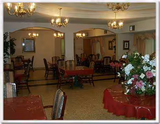 Indoor dining room at Evangeline Oaks Guest House with chandeliers, red tablecloths, and wooden chairs.