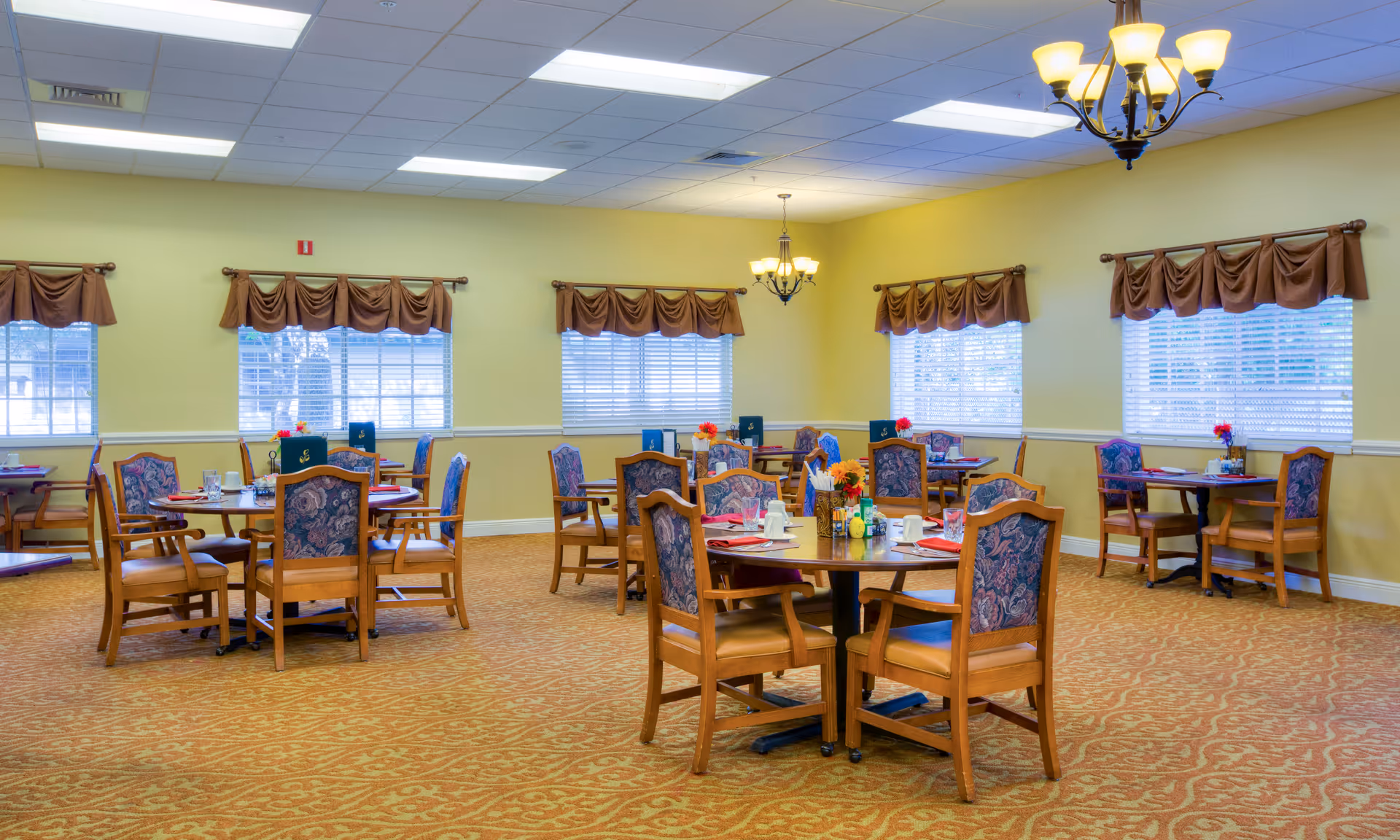 Bright senior living dining room with round tables and wooden chairs set for meals