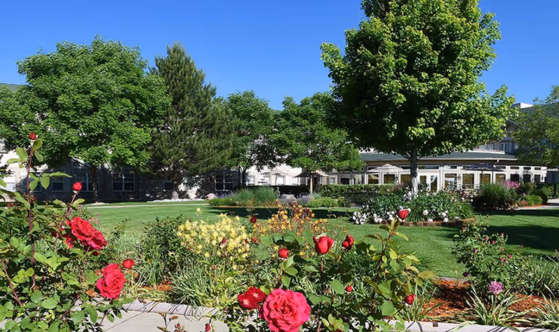 Sunny landscaped courtyard with red roses, green lawns, and the facility building in the background.