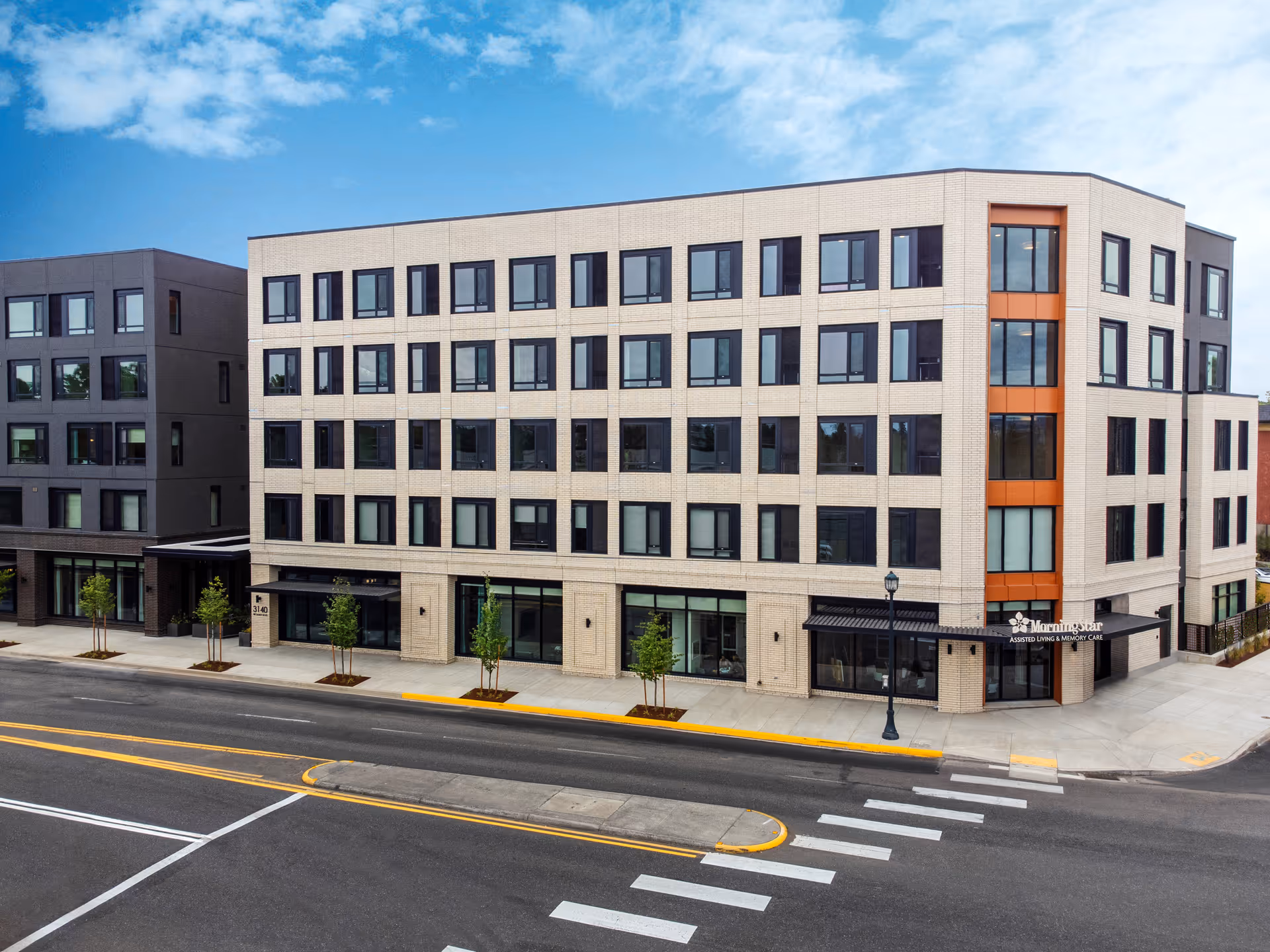 Front exterior view of a multi-story MorningStar Assisted Living & Memory Care building with rows of windows and a corner entrance facing a city street.