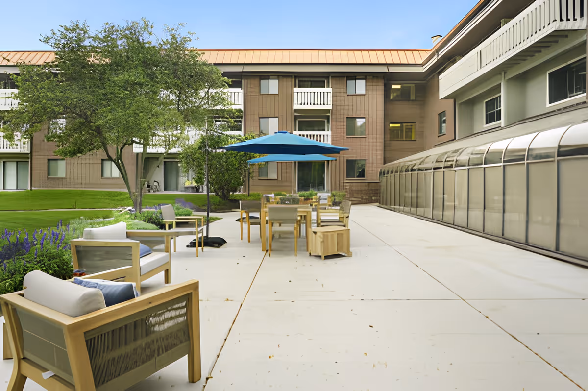 Outdoor courtyard patio with seating, tables and a blue umbrella between multi-story building wings.