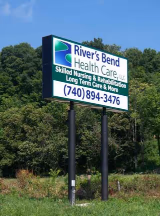 Outdoor sign for River's Bend Health Care with phone number, amid trees.
