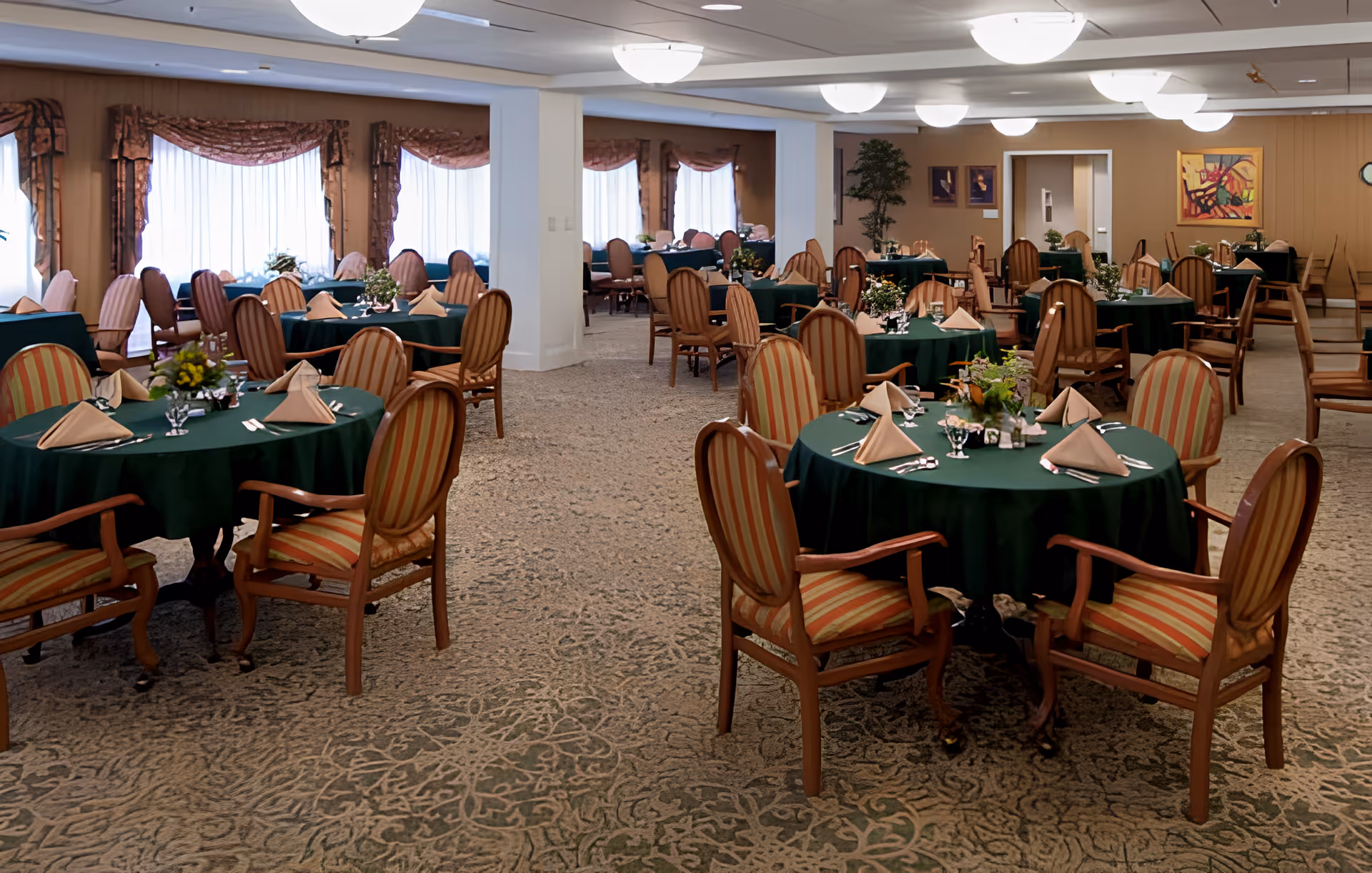 Spacious dining room with round tables covered in green tablecloths, place settings and wooden chairs.