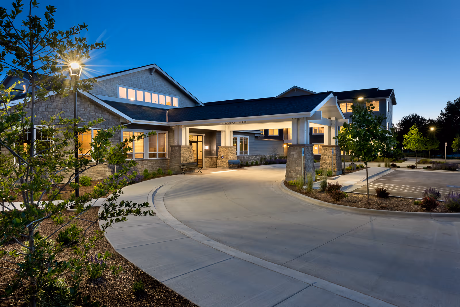 Revel Eagle senior living facility entrance with curved driveway, stone pillars, and illuminated windows at dusk