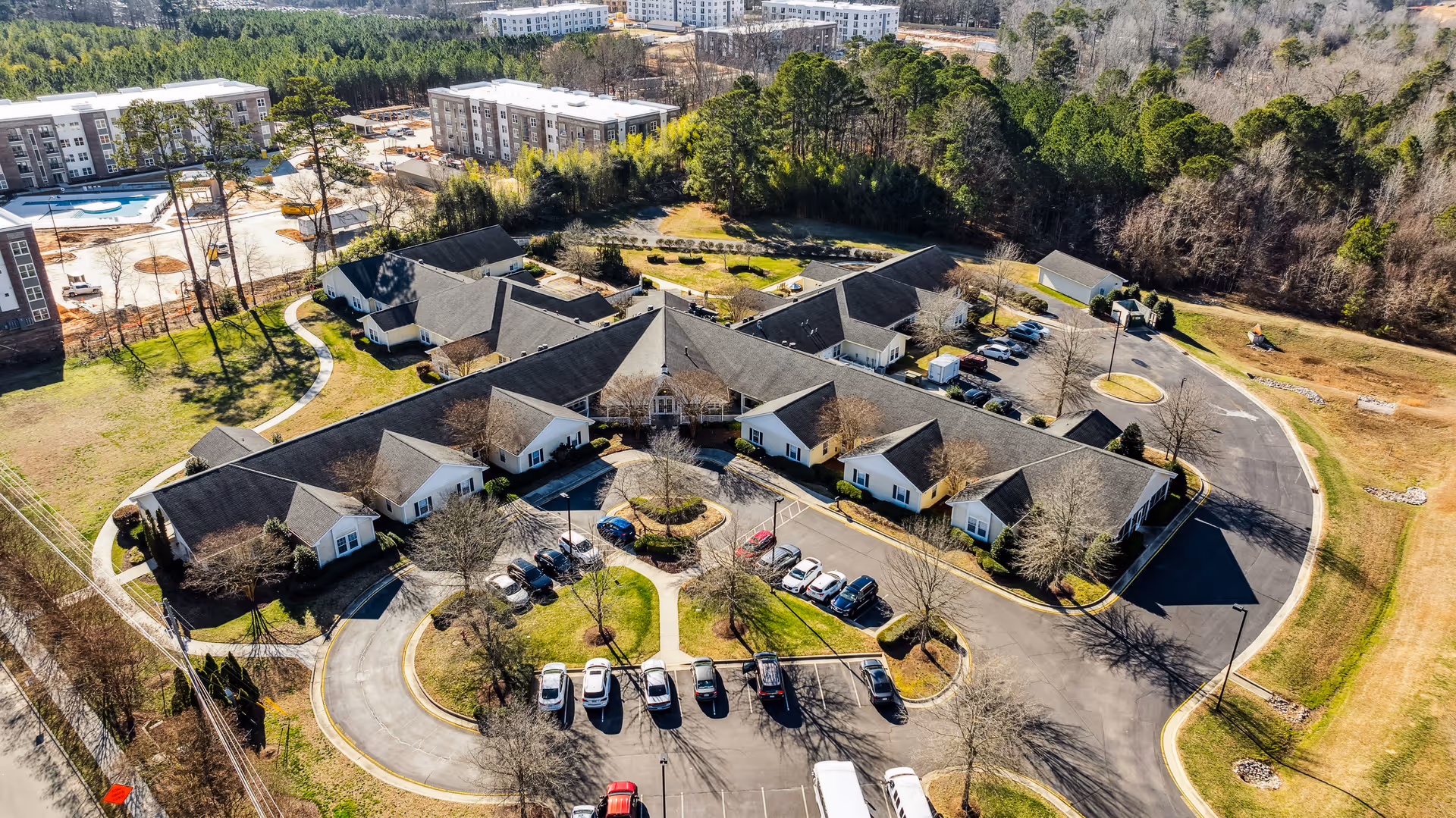 Aerial view of a single-story senior living facility arranged around a circular driveway and parking lot, surrounded by trees and nearby buildings.