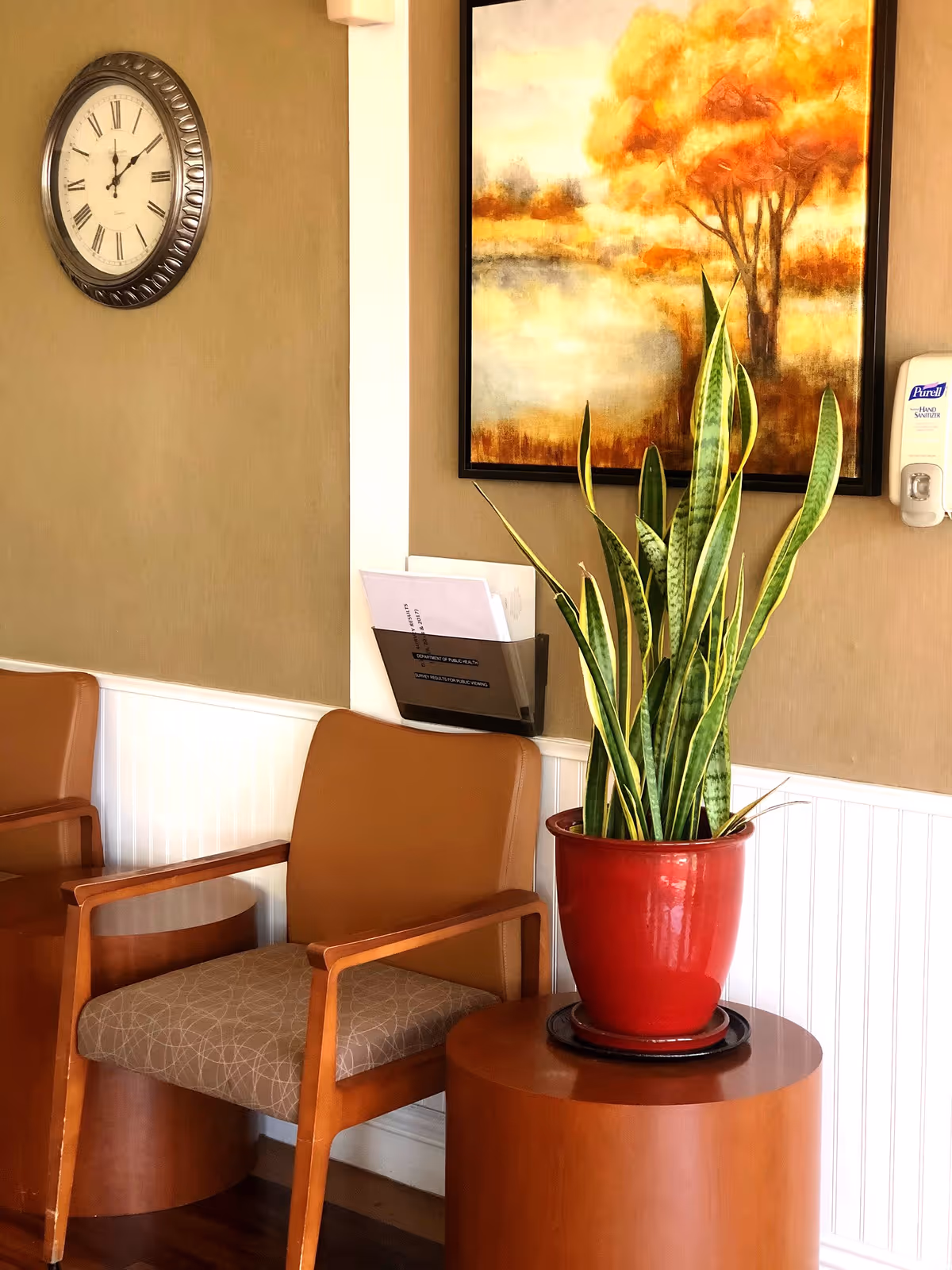 A cozy waiting area with two chairs, a plant, a clock, and an artwork on the wall.