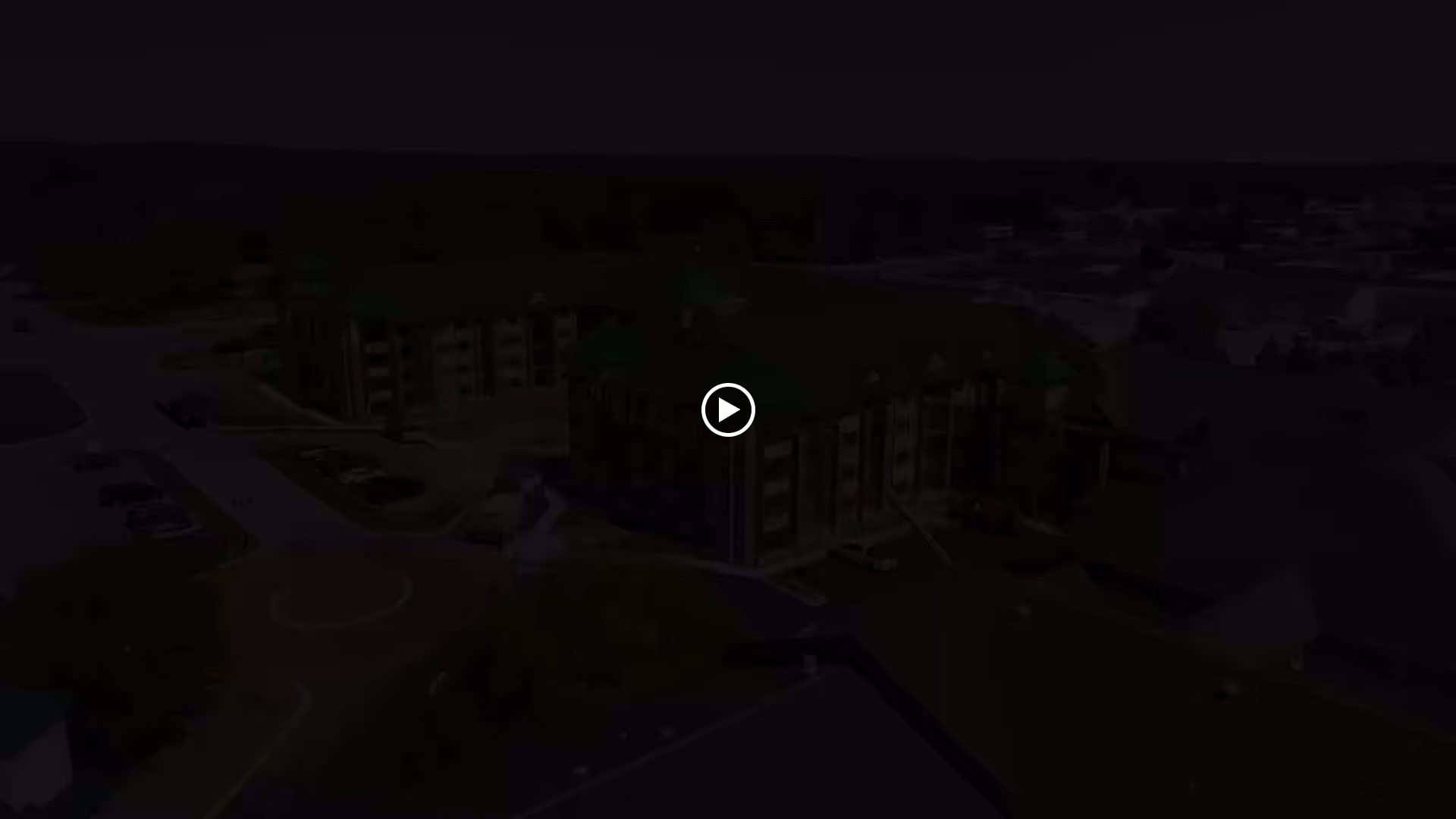 Aerial view of Forest Ridge Senior Community showing multiple connected buildings with green roofs, surrounding parking lots, and nearby roads in a suburban area.