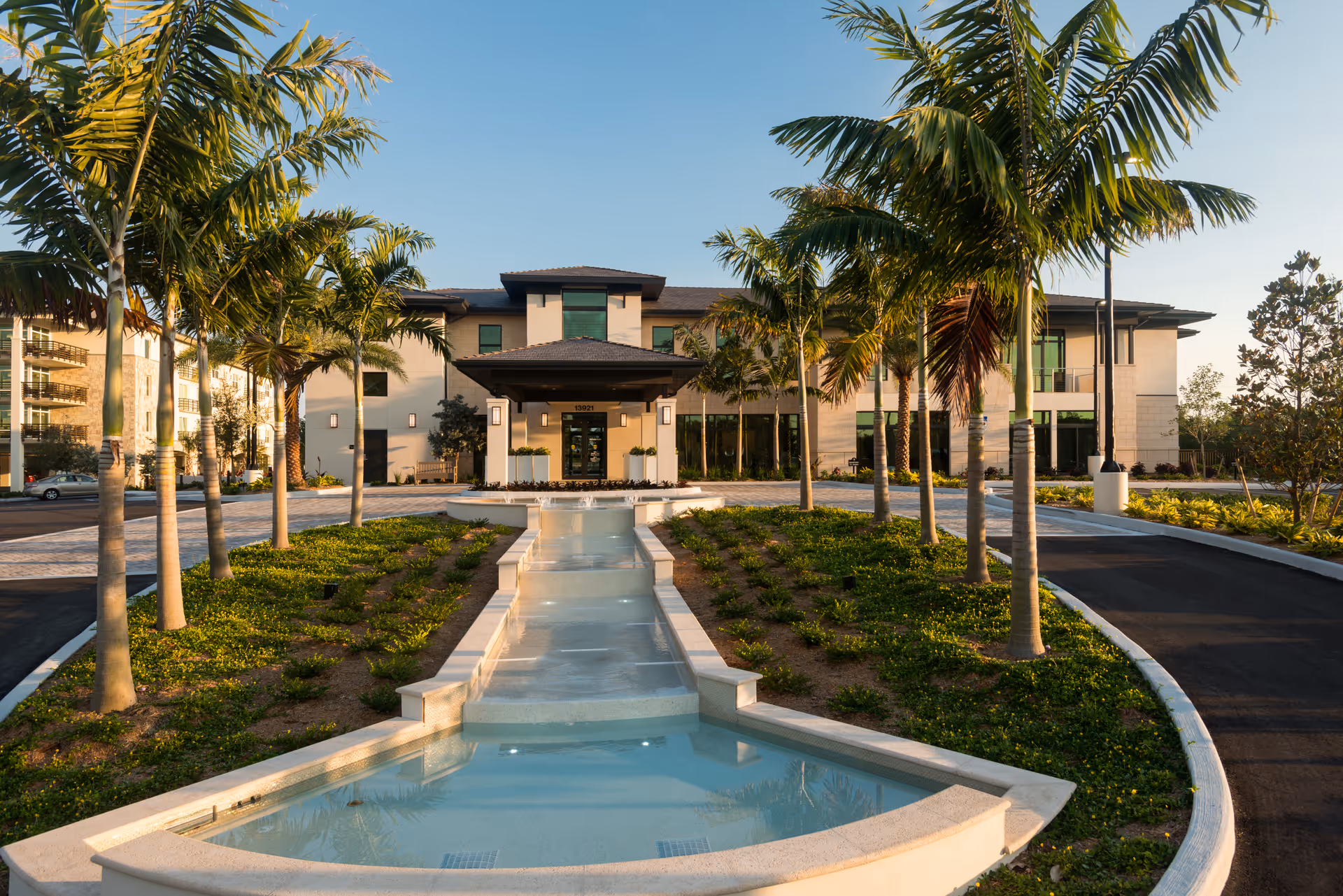 Front exterior view of the Shell Point Welcome Center building with a landscaped driveway lined with palm trees and a decorative water feature in the center.