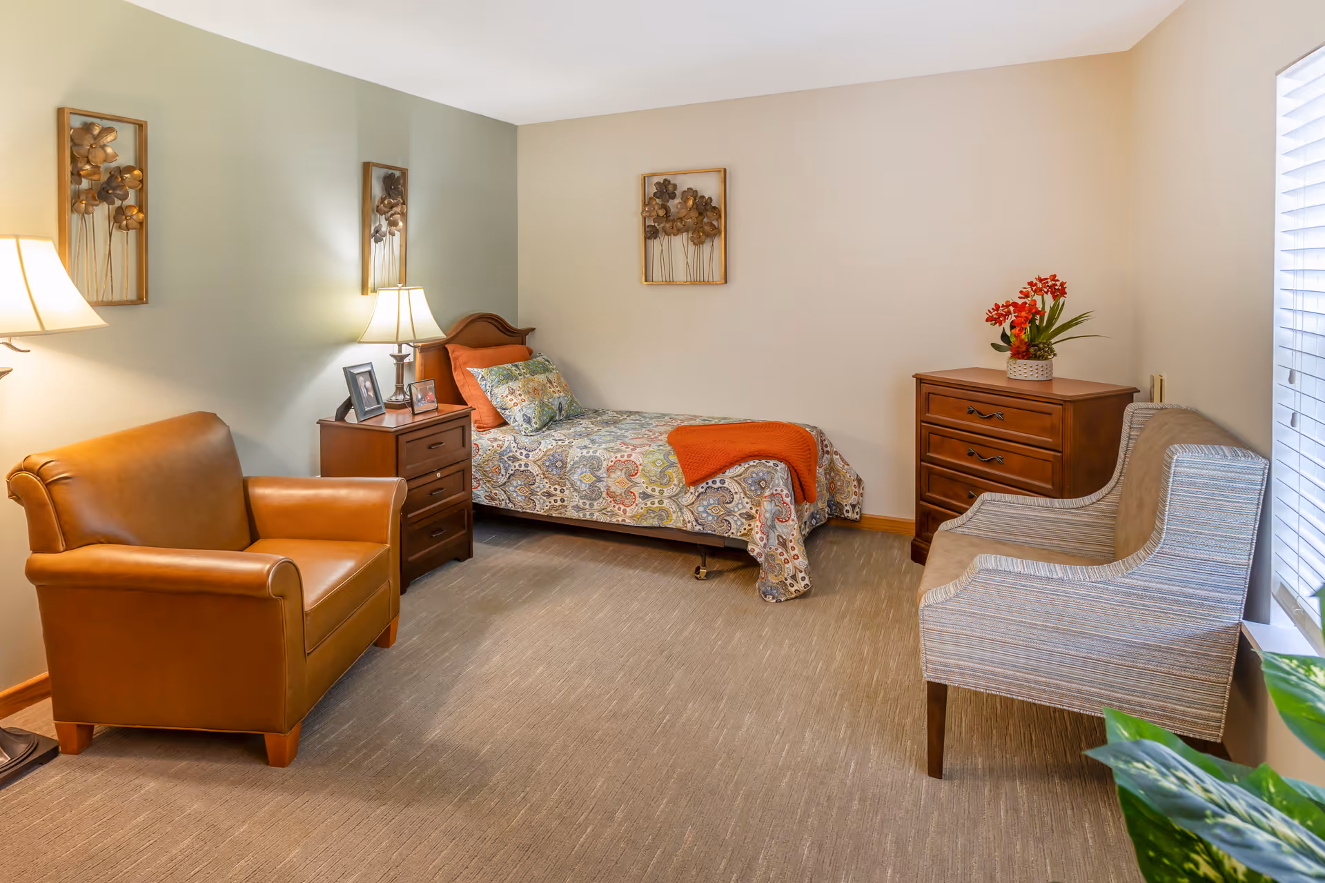 Light-filled furnished bedroom with a single bed, two armchairs, a nightstand and a dresser.