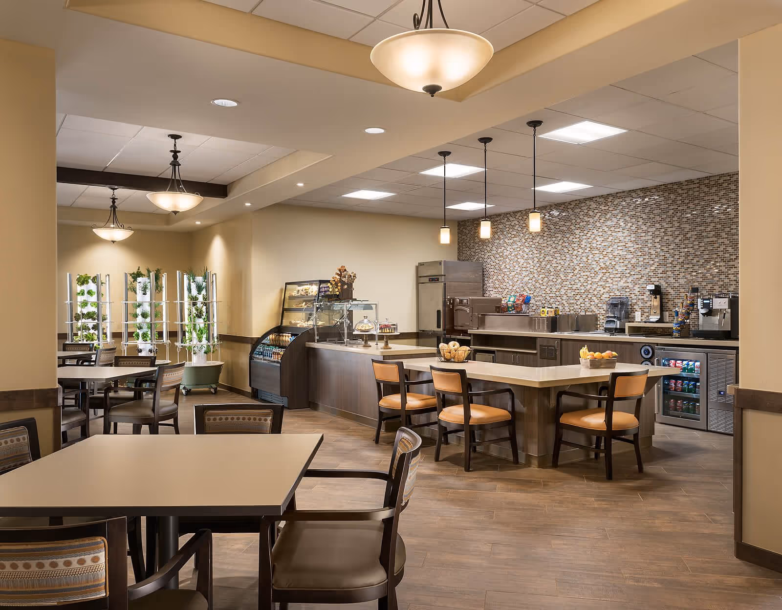 Bright communal dining and café area with tables, chairs, a central island, and a service counter in a senior living facility.