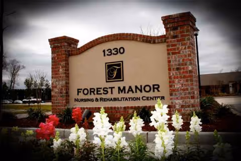 Forest Manor entrance sign with brick pillars and blooming flowers in front