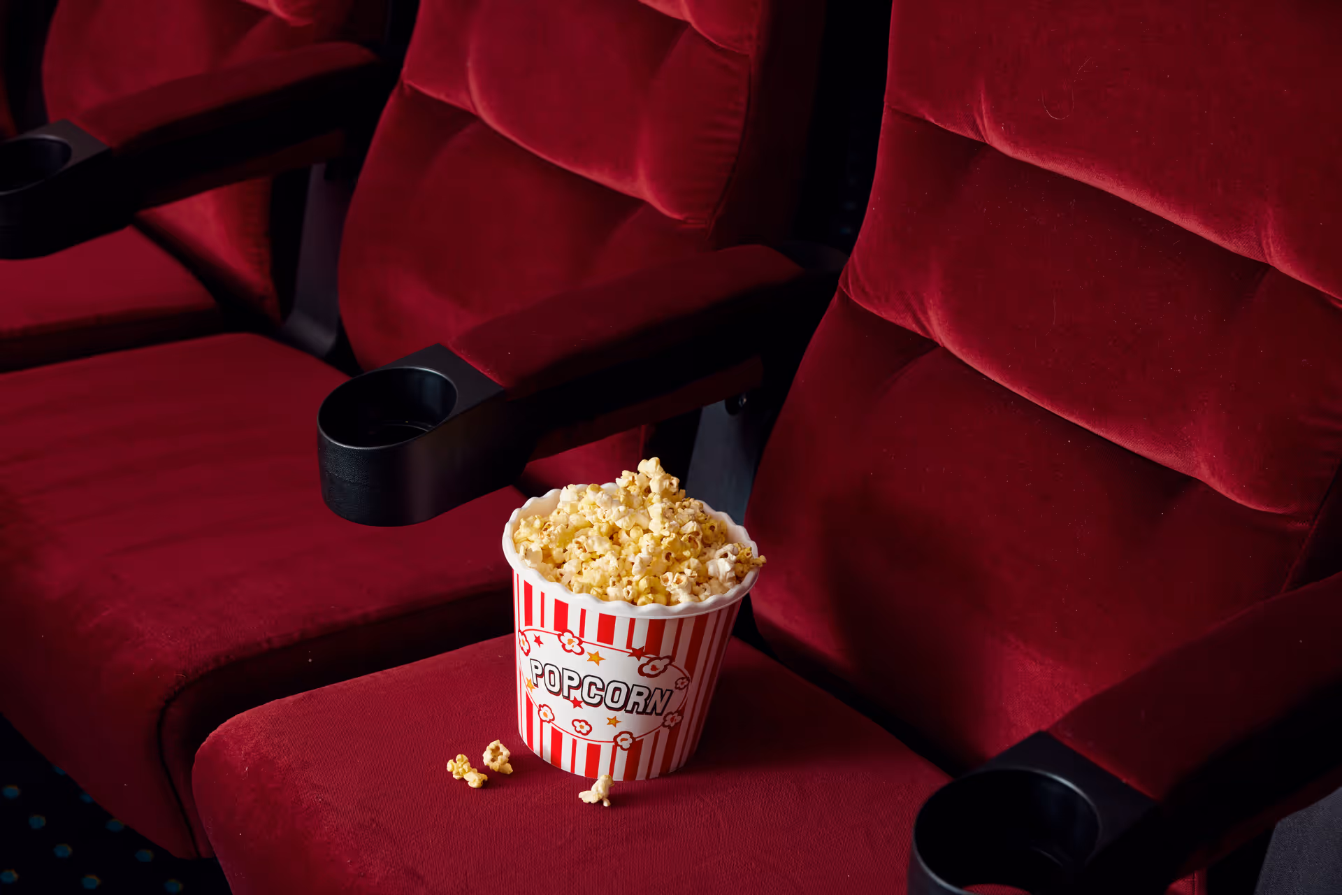 A bucket of popcorn placed on a red velvet theater seat with adjacent similar seats visible.