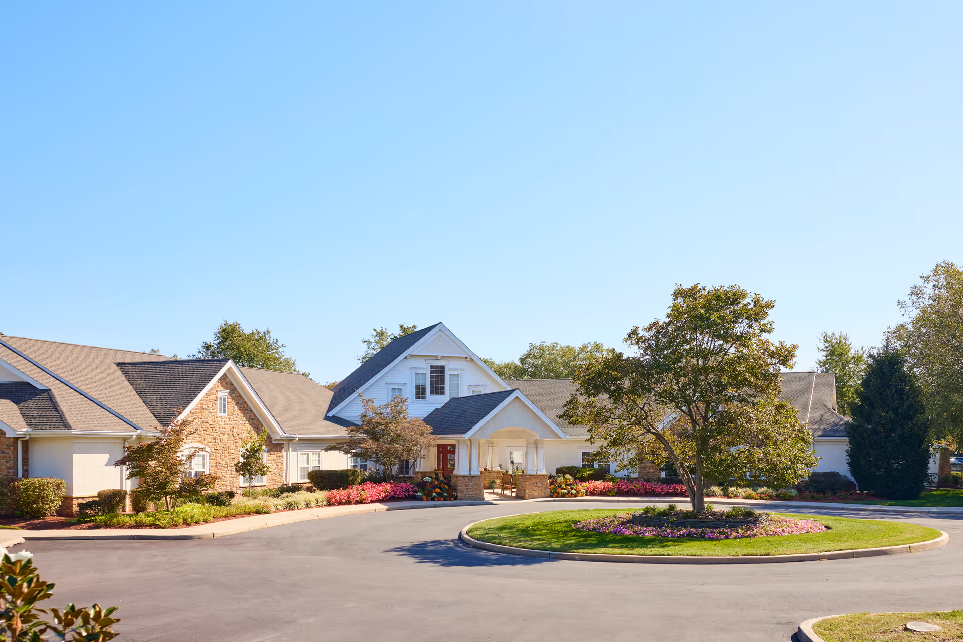 Front exterior of a senior living building with a covered entrance, circular driveway, and landscaped grounds.