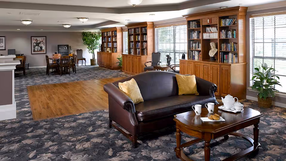 Spacious lounge with a leather sofa and coffee table set for tea, built-in bookshelves, tables and large windows.