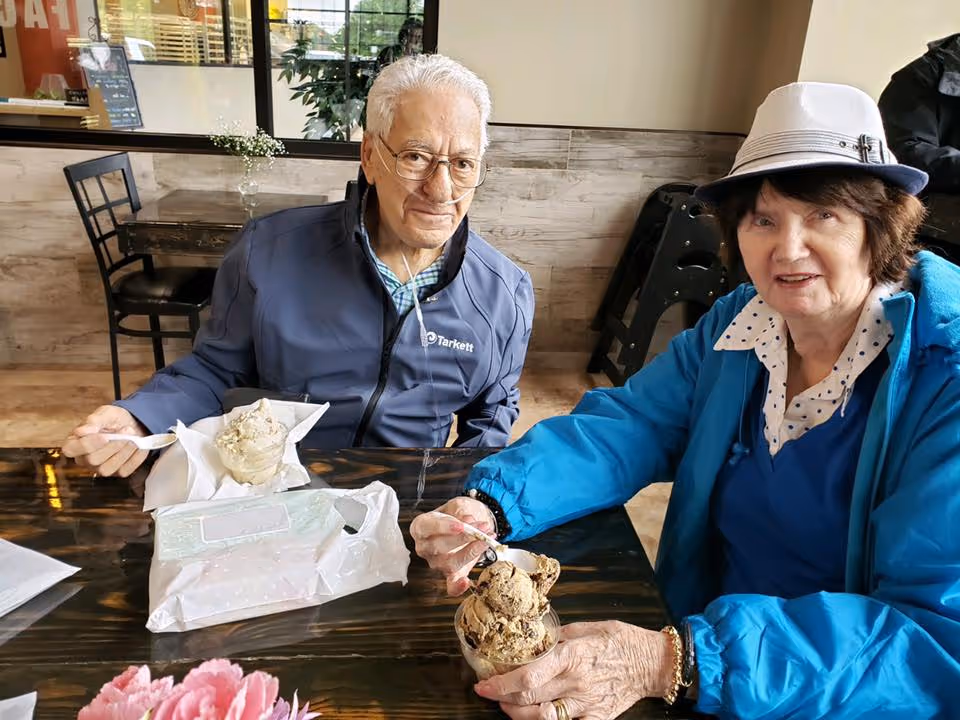 Two older adults seated at a table indoors enjoying ice cream.