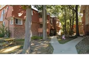 Brick multi-unit apartment building exterior with trees, a sidewalk, and a picnic table in the courtyard.