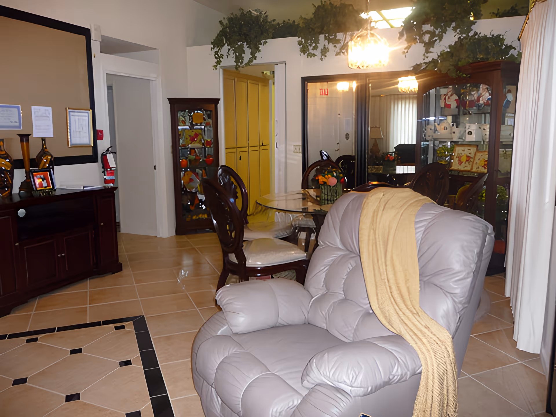 Interior living area with a large leather recliner draped with a blanket, a glass dining table and chairs, and cabinets with decorative items.