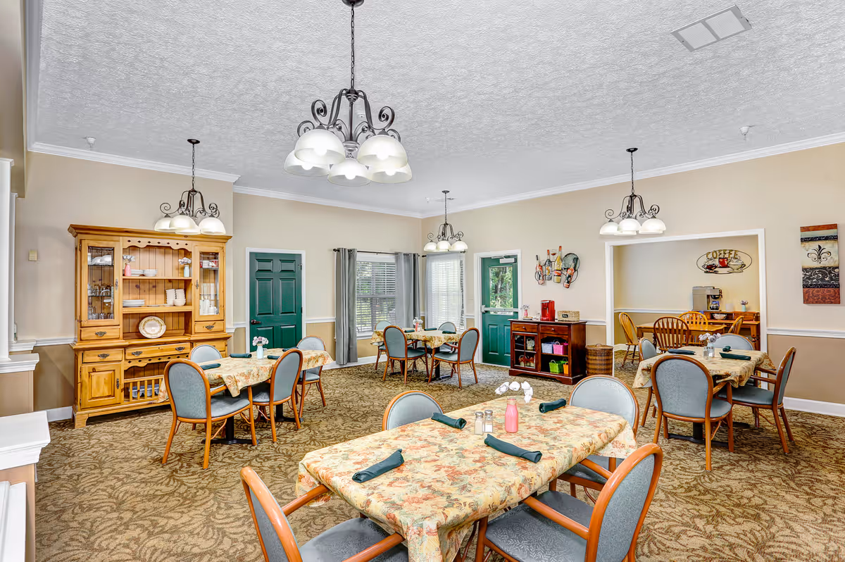Bright dining room with several set tables and chairs, a wooden hutch, chandeliers, and green doors.