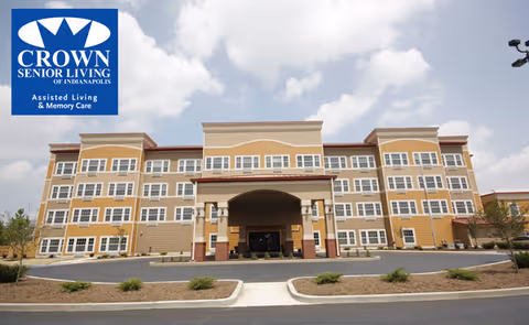 Four-story Crown Senior Living building with a covered entrance, driveway, and landscaping under a partly cloudy sky.