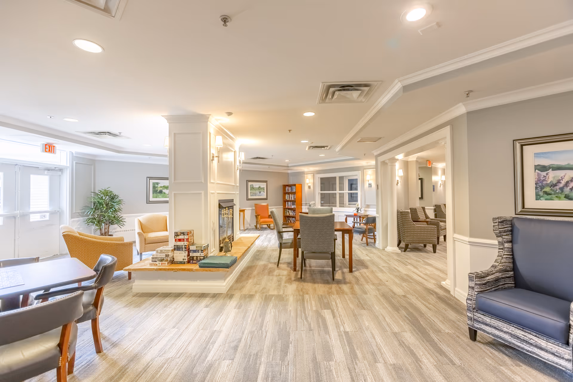 Bright, spacious senior living common area with seating, tables, a fireplace and bookshelves.