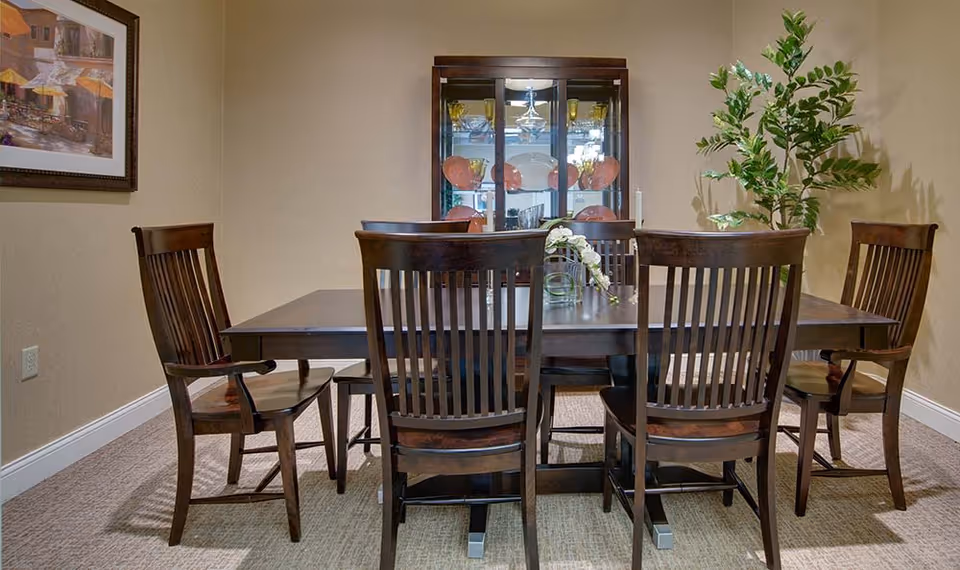 Dining room with a dark wooden table and six chairs, a china cabinet and a potted plant against beige walls.
