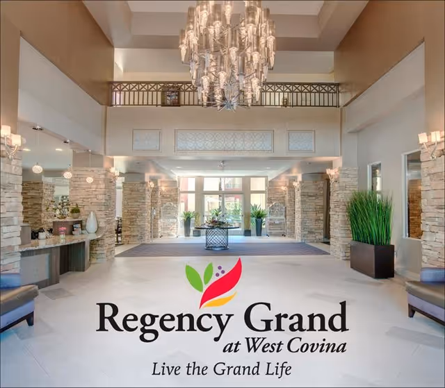 Spacious and elegant lobby area of Regency Grand at West Covina featuring a large chandelier, stone pillars, modern seating, and decorative plants with natural light coming through large windows.