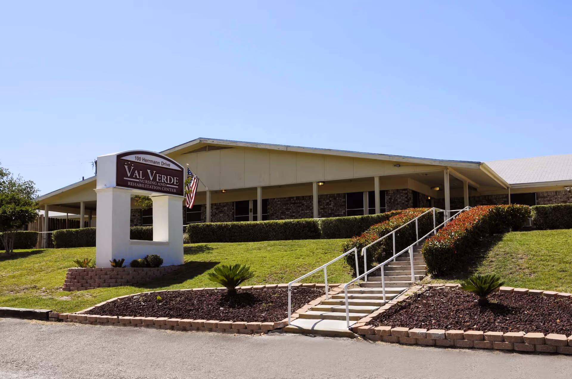 Front exterior of the Val Verde Nursing and Rehabilitation Center showing the building, entrance stairs, and a sign on the lawn.