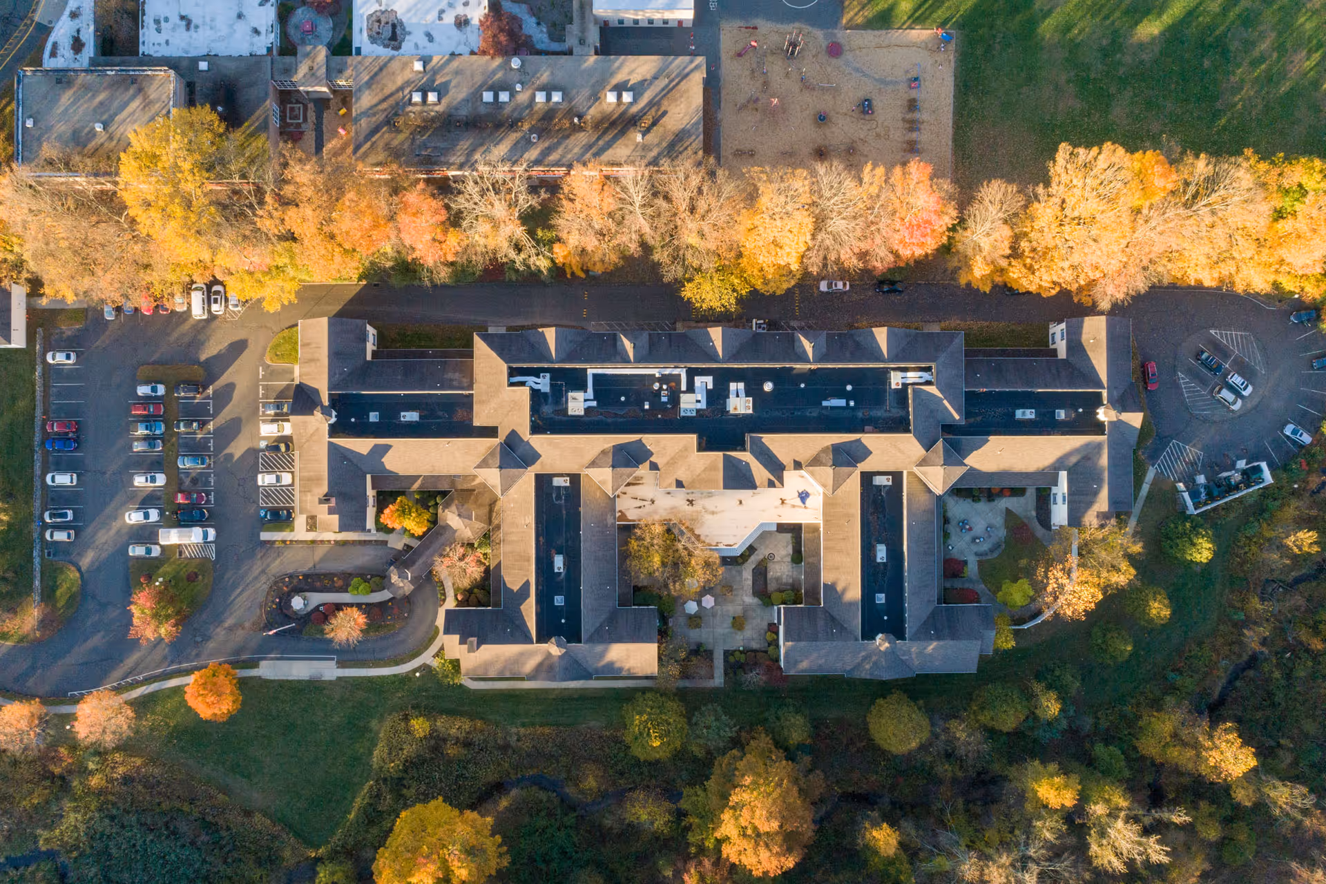 Aerial view of Monarch Southbury facility surrounded by trees with autumn foliage, parking lots with cars, and green landscaped areas.