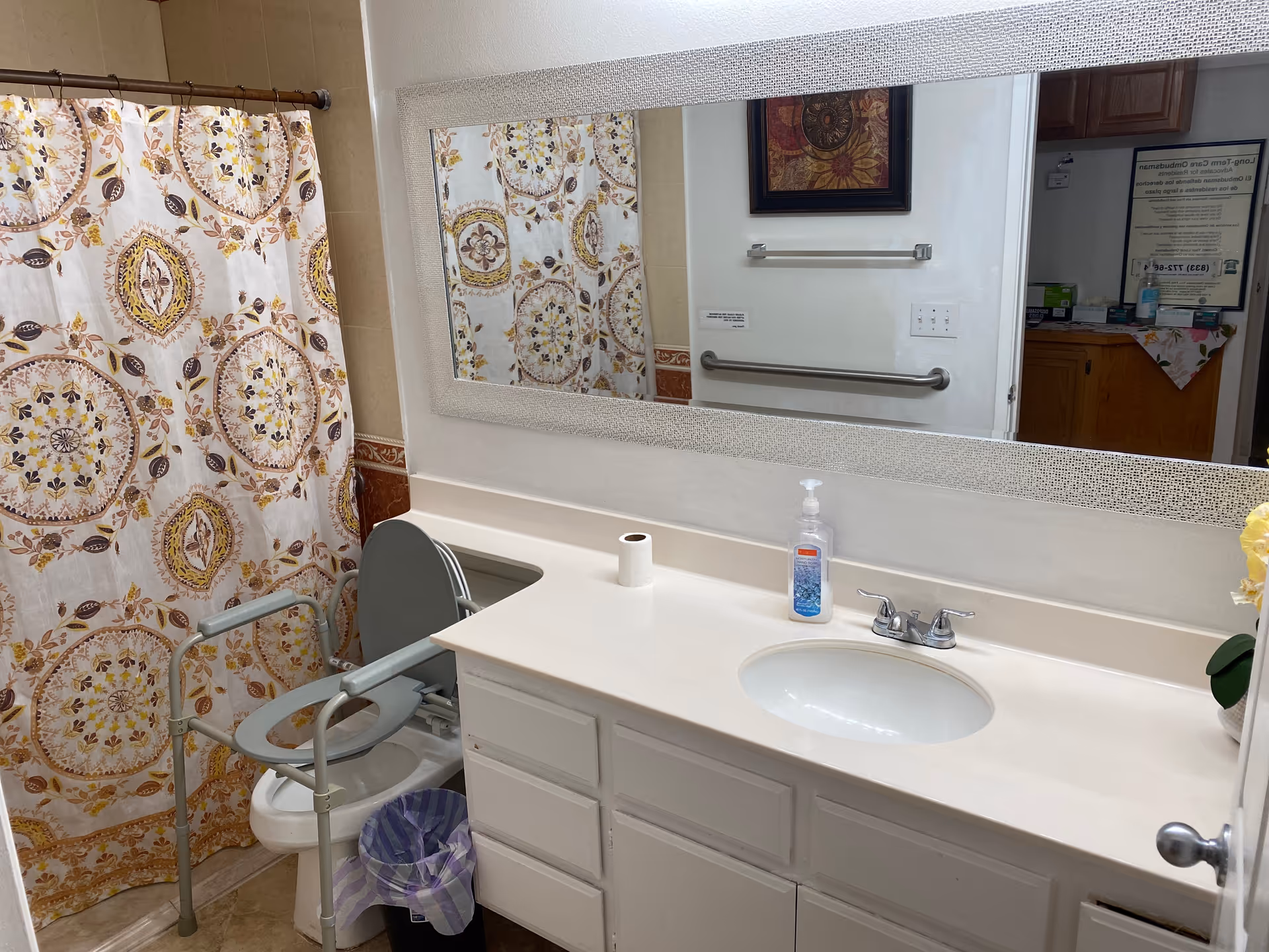 Accessible bathroom with shower curtain, toilet, sink, and safety rails in a senior facility.