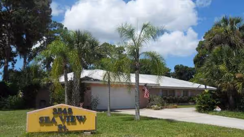 Front view of Sea View Inn at Forest Lakes with a sign, palm trees, and sky.